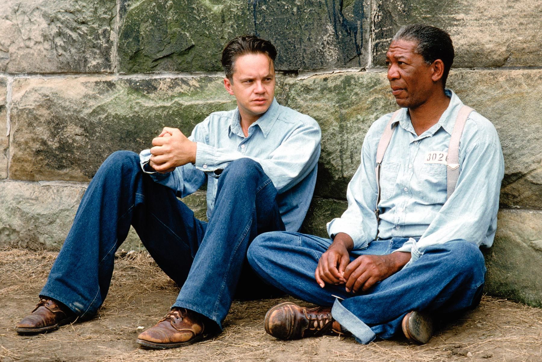 Andy Dufresne (Tim Robbins) and Ellis 'Red' Redding (Morgan Freeman) sitting against a stone wall in Shawshank Prison, deep in conversation about hope and freedom.