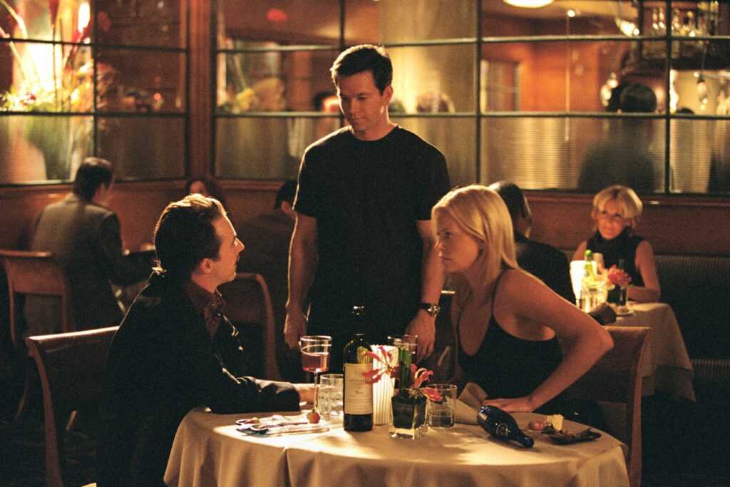 Charlie Croker (Mark Wahlberg) confronts Steve (Edward Norton) in a tense restaurant scene from The Italian Job (2003). Stella Bridger (Charlize Theron) looks on, realizing the betrayal that led to their mentor’s death