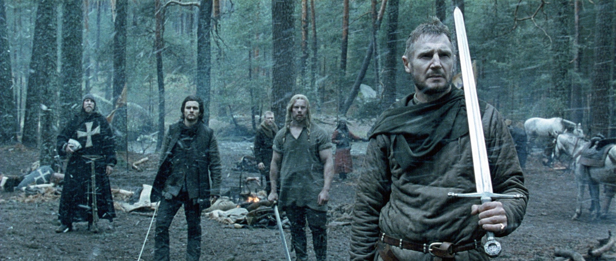 iam Neeson as Godfrey of Ibelin stands in a dense, snow-covered forest, gripping his sword as his men, including Orlando Bloom’s Balian, prepare for an ambush. This pivotal moment marks Balian’s first step toward his destiny as a knight, setting the stage for his transformation.
